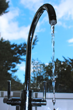 Tap with flowing water in front of window to blue sky